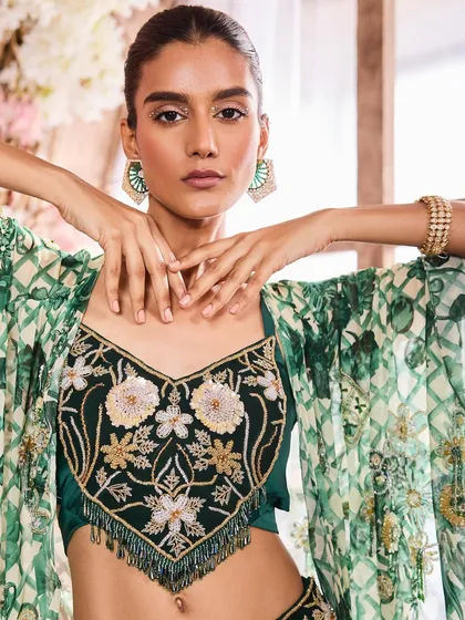 A stunning close-up of a model in an embroidered green blouse. The makeup features a subtle winged liner and glowing skin, highlighting the model's features beautifully.