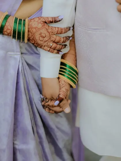 A close-up of the couple holding hands, showing the beautiful details of the bride's engagement mehndi. The rich stain looks stunning against her lavender saree.