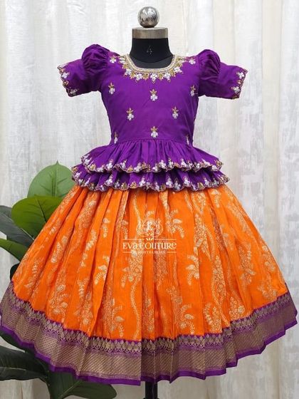 A striking color combination of purple and orange. This peplum Pattu Pavadai features delicate embroidery on the blouse and a rich Banarasi silk skirt.