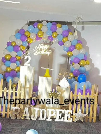 A colorful balloon arch with purple, blue, gold, and white balloons. The "BABY" blocks and light-up name make it a fun and festive setup for a 2nd birthday.