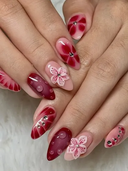 Blooming in bold shades of red. This dramatic set features 3D pink sakura flowers, deep red blooming gel effects, and sparkling water droplet accents for a truly unique look.