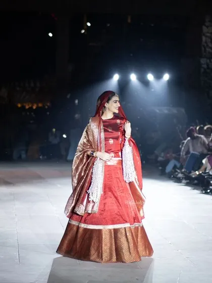 Kriti Sanon walking the ramp at the 'Dharohar Kashi Ki' show. The spotlights highlight the intricate details of her outfit against the dark, atmospheric background.