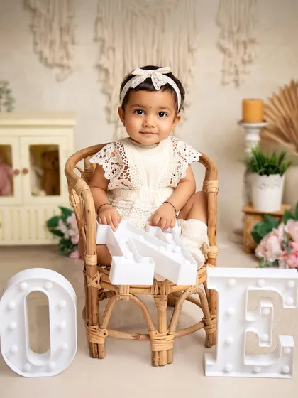 One year old and sitting like a queen. This portrait uses a beautiful rattan chair and light-up letters to create a stylish and memorable first birthday photo.