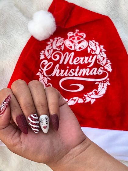 A full set of Christmas-themed press-on nails. This fun design includes matte red, candy cane stripes, a cute reindeer face, and a textured sweater pattern for a cozy winter look.