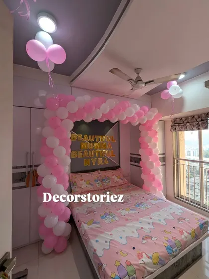 A sweet and simple bedroom decoration to welcome a new baby or for a birthday. This setup features a pink and white balloon arch over the bed, creating a lovely frame.