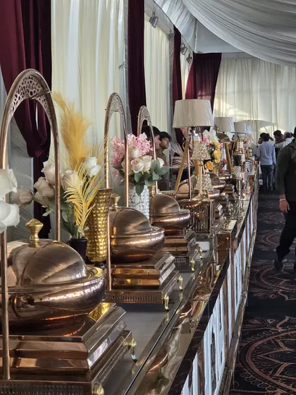 An elegant buffet line from a recent wedding we catered. The setup features our premium copper-toned chafing dishes, beautiful floral arrangements, and ambient table lamps, creating a warm and inviting dining experience for guests.