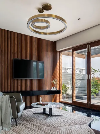 This lounge area opens onto a terrace, blending indoor and outdoor living. The feature wall of vertical timber slats adds warmth and texture, complemented by a modern circular chandelier and marble-topped coffee table.