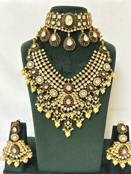 A heavy bridal necklace set with a wide, web-like design. This rental piece is adorned with Kundan, pearls, and Meenakari work.