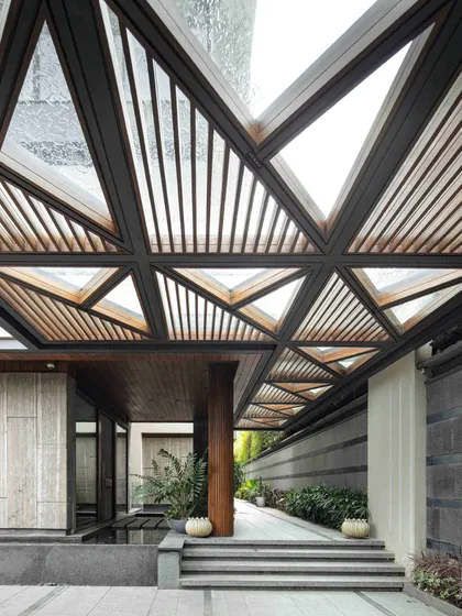 The entrance to the Bammi Residence is designed as a dramatic transition from the urban exterior to a serene interior. The geometric, slatted canopy filters natural light, creating dynamic patterns of light and shadow on the steps and water body below. This architectural feature sets a tone of thoughtful design and a deep connection to natural elements, which is a hallmark of our work.