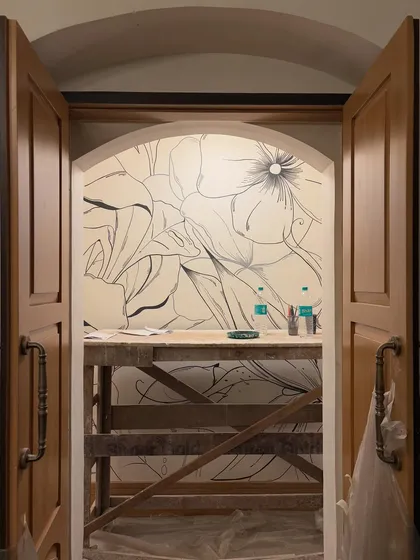 The beginning of a monochrome floral mural, seen through an arched doorway. This work-in-progress shot captures the anticipation of a blank wall about to bloom with art.