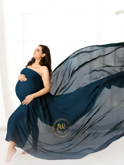 A dynamic solo portrait using a flowing teal fabric. The fabric is tossed to create a wave-like effect, highlighting the mother's silhouette against a clean, white background.