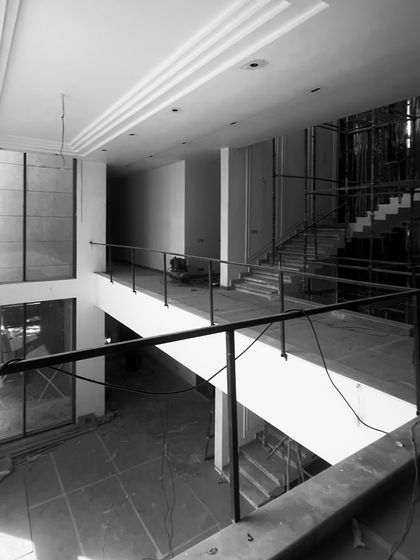The interior of a double-height living room during construction. Even with bare walls and scaffolding, the grand scale, tall windows, and ceiling details hint at the bright, open, and dramatic space it is planned to become.