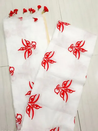 A close-up of a white saree featuring red embroidered motifs of the goddess's eyes, a symbolic design for Durga Puja. The pallu is finished with small red tassels.