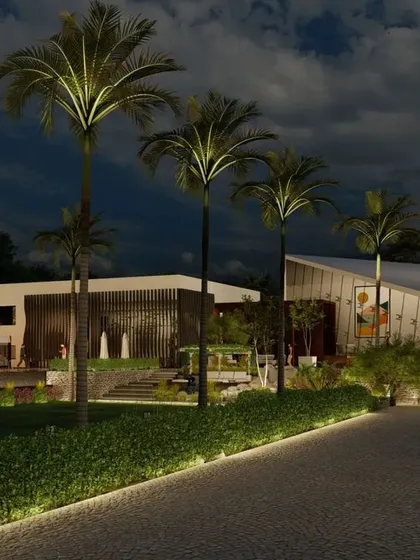 The grand entrance to the farmhouse at night. The illuminated driveway leads towards the strikingly modern buildings, with landscape lighting highlighting the palm trees and manicured lawns, creating a luxurious and welcoming arrival experience.
