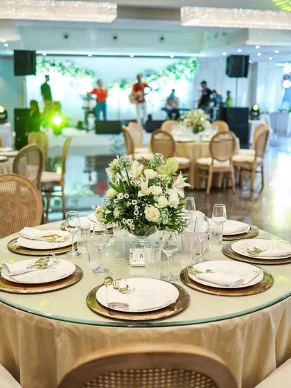 An elegant round table setting with gold charger plates and a beautiful white floral centerpiece. In the background, a live band sets the mood, showcasing how our catering integrates seamlessly with other event elements.