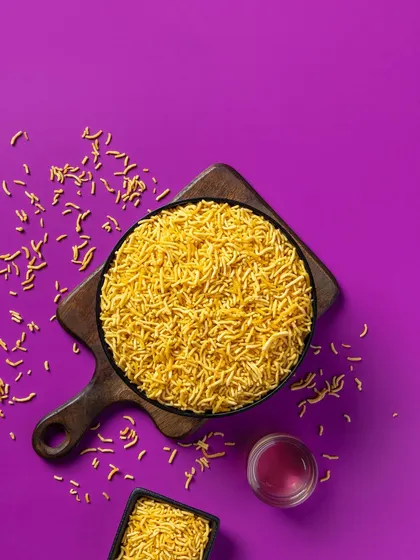 A vibrant shot of Aloo Bhujia against a solid purple background. This type of high-contrast, colorful food photography is designed to grab attention on retail shelves and online.