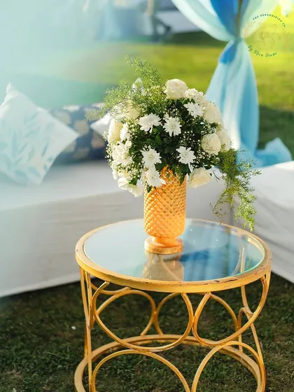 A simple yet beautiful detail for an outdoor mehndi-sangeet. A gold vase with a bouquet of white chrysanthemums on a mirrored side table adds a touch of sunny elegance.