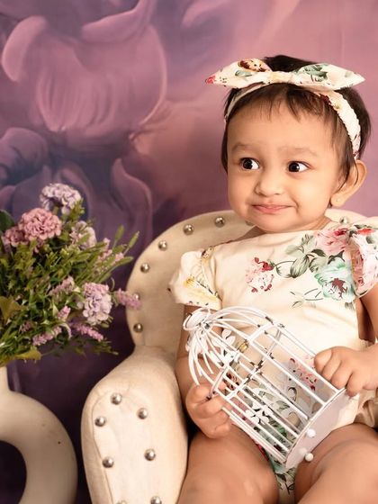 A sweet, curious expression captured in our lavender-themed setup. The birdcage prop adds a touch of whimsical charm to the portrait.