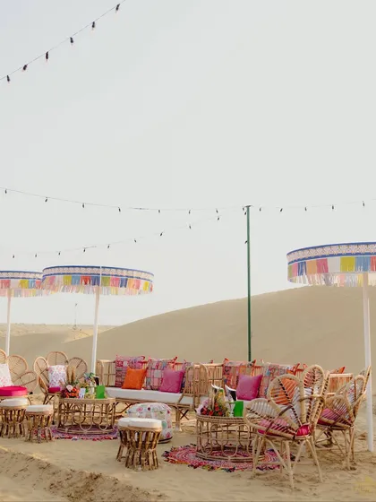 Multiple lounge areas set up on the desert dunes for the Mehendi. The colorful umbrellas and rattan furniture created a festive, bohemian vibe against the vast, sandy landscape.