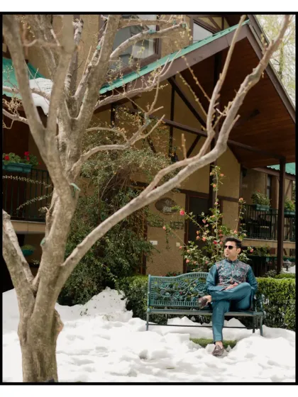 A portrait of the groom, seated on a bench surrounded by snow. It's a relaxed, candid style shot that captures his personality and the unique winter setting of the Manali wedding.