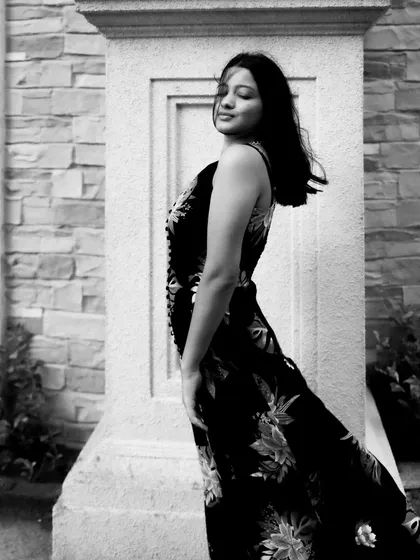 A black and white portrait using natural light and a stone pillar for framing. The motion in the model's hair adds a dynamic, candid feel to the shot.
