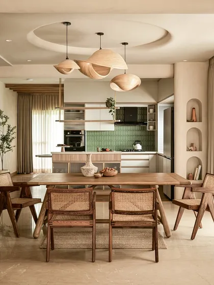 I design open-concept spaces where life flows seamlessly from one moment to the next. This view connects the dining area to the kitchen, unified by sculptural wooden pendant lights, natural materials like cane and teak, and architectural details like the recessed ceiling, demonstrating a complete and cohesive home vision.
