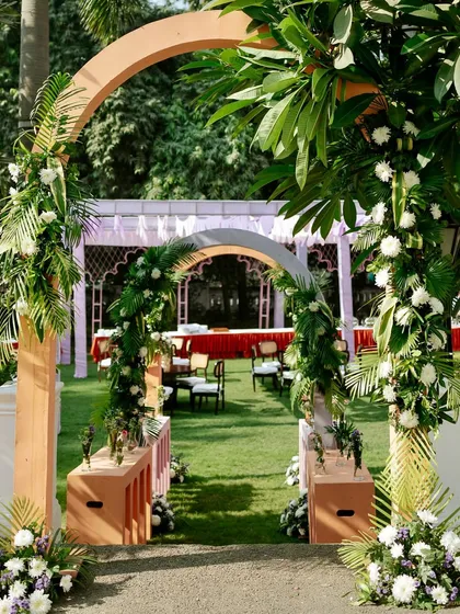 A lush green entranceway for the Mehendi, with simple wooden arches wrapped in tropical leaves and white flowers, creating a natural and organic feel.
