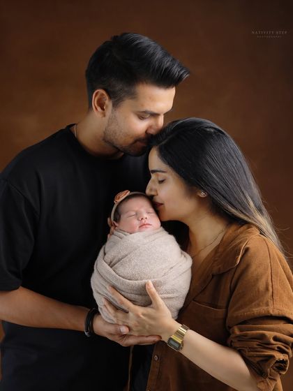 The complete family. A father’s gentle kiss on the mother’s forehead while she holds their newborn creates a portrait filled with love, protection, and tenderness.