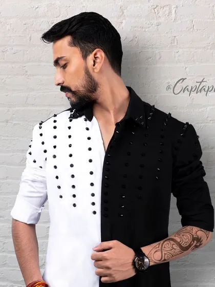 This image showcases an edgier style of men's fashion photography. Shot against a textured brick wall in the studio, the focus is on the unique design of the split black-and-white shirt and the model's strong profile.