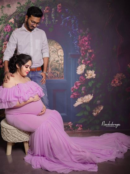 A tender moment between an expecting couple in the studio. The lavender gown and floral backdrop create a soft, romantic atmosphere.