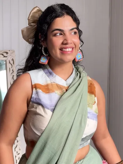 A smile is your best accessory, but a cute bow and fun earrings are a close second. This look combines a printed sleeveless blouse with a simple green saree, showing how you can mix and match pieces to create new outfits.