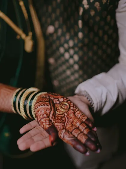 A symbolic shot of the engagement ring placed in the bride's henna-decorated hand. This close-up highlights both the modern commitment and the traditional artistry of the occasion.