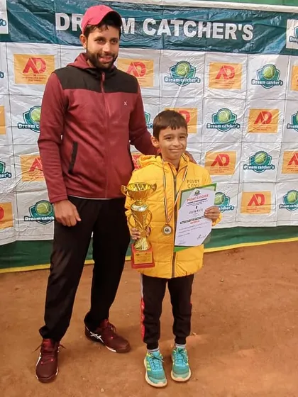 One of our U10 champions from the Saket center posing with his coach and trophy at the Dream Catcher's tournament. His bright yellow jacket is as vibrant as his winning spirit.