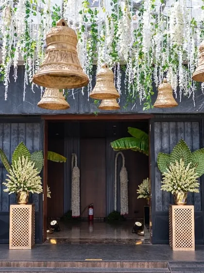The entrance to a wedding venue, decorated with hanging temple bells and traditional floral arrangements.
