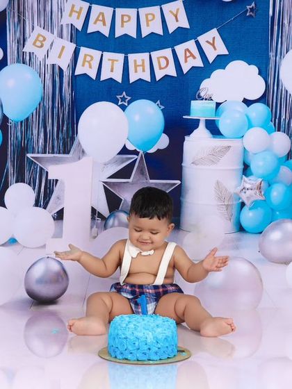 A fun moment captured as the birthday boy dives into his blue cake. This action shot shows the playful and messy side of a classic cake smash session.
