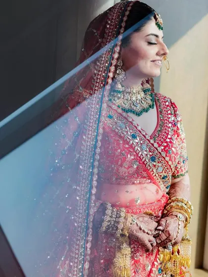 An artistic shot of a bride through a reflection, her red lehenga and green-beaded Kundan jewellery creating a beautiful, timeless image.