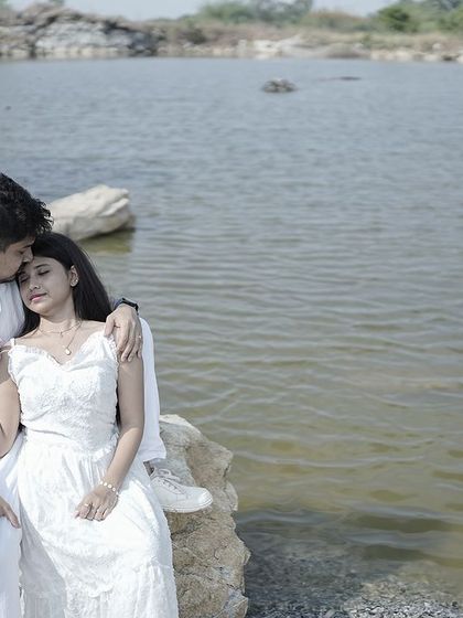 A romantic moment with the groom kissing the bride's forehead as she rests her head on his shoulder, by a lake.