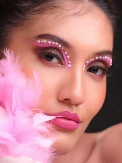 A fun, vibrant editorial look using pink tones and face gems. The double bun hairstyle adds a playful touch.