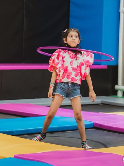 A young girl having a blast with a hula hoop on a trampoline at a superhero-themed party. This is a perfect picture of active, happy fun.
