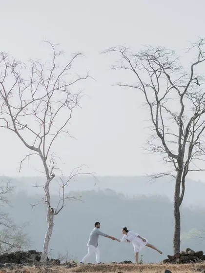A wide, scenic shot of a couple on a hilltop, framed by bare trees against a hazy sky. This image showcases my love for using natural landscapes to create epic, breathtaking couple portraits.