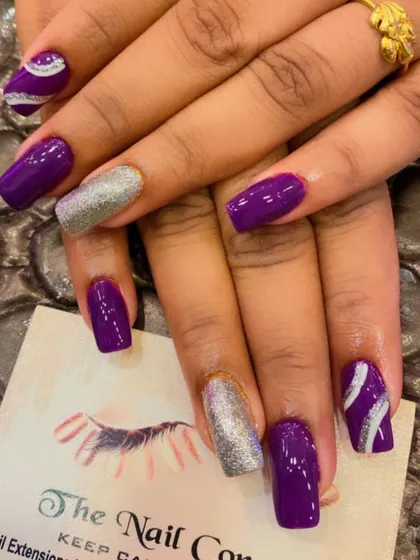 A bold and glossy set of square nails. The deep purple polish is paired with silver glitter accent nails and purple nails with a silver swirl design.