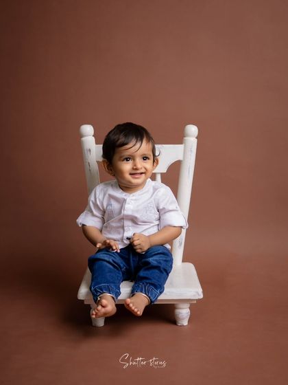 A simple and classic portrait of a toddler boy in a white shirt and jeans, sitting on a small white chair.