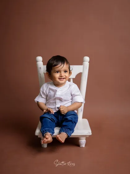 A simple and classic portrait of a toddler boy in a white shirt and jeans, sitting on a small white chair.