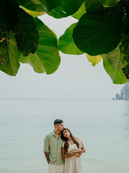 A beautifully framed portrait from a post-wedding shoot in Phuket. The large green leaves create a natural canopy over the couple, drawing focus to their intimate embrace against the tranquil sea.
