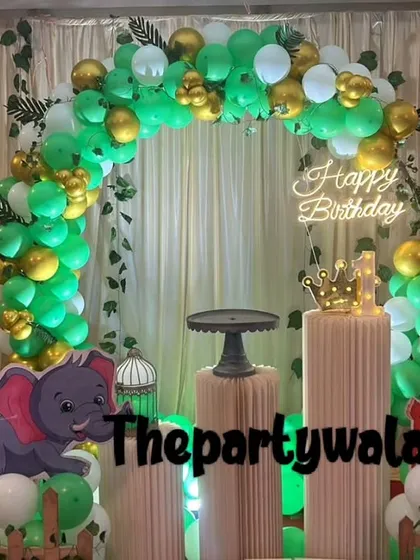 A simple jungle theme with a green, gold, and white balloon arch against a curtain backdrop. The tiger, elephant, and deer cutouts add to the wild fun.