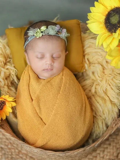 This little one is wrapped in a warm yellow swaddle, sleeping peacefully among sunflowers.