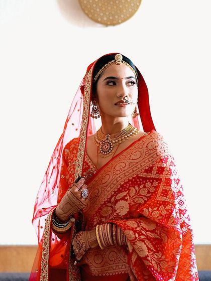 A classic portrait of a bride in a traditional red Banarasi saree, looking away with a regal and poised expression.