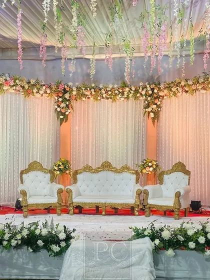 An elegant and classic wedding stage in white and pastel tones. I used flowing drapes, a ceiling of hanging flowers, and a pristine white sofa set for a dreamy, ethereal vibe.