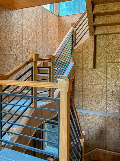 This multi-story staircase combines sturdy wooden posts with sleek metal railings, set against textured OSB walls. It's a functional design element that adds to the rustic yet modern aesthetic.