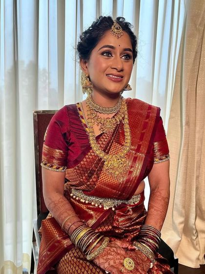This bride's look is all about traditional elegance. The makeup is flawless and matte, providing the perfect canvas for her heavy temple jewellery and rich red saree.